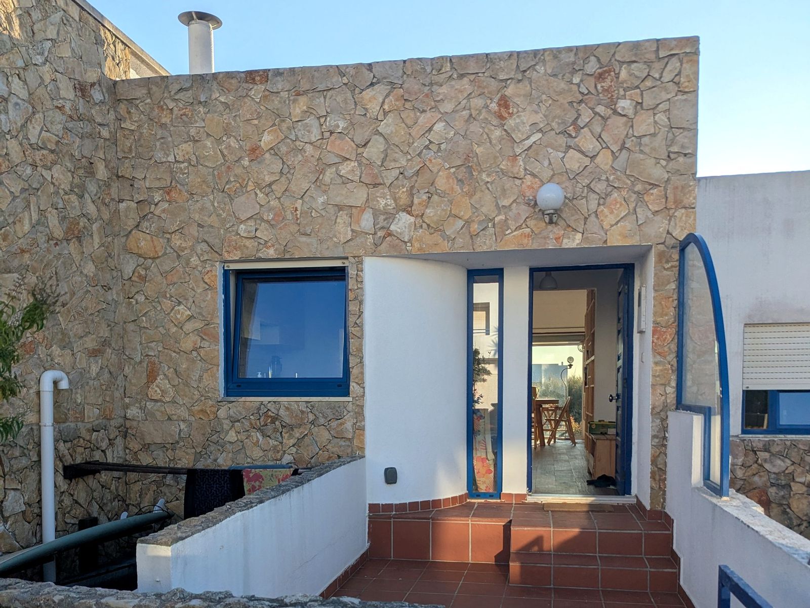 The front of the house, stone with blue-painted trim and the door open.