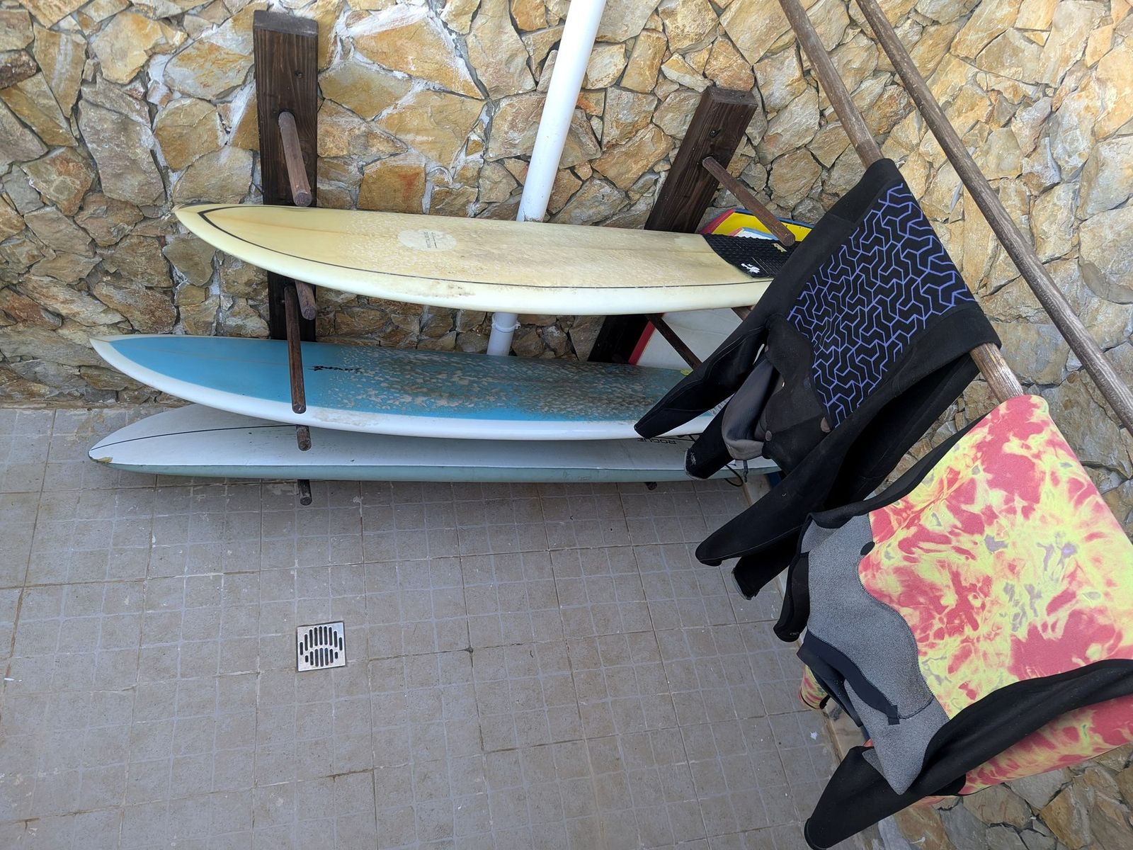 Surfboards on a wall rack, wetsuits hanging alongside.